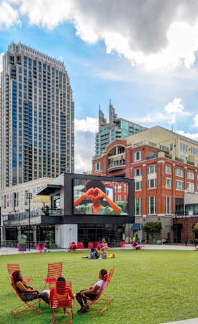 A park with people sitting on chairs and a tall building in the background.