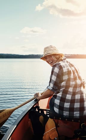 A person wearing a hat is paddling a canoe on a lake at The Villas at Sand Lake Resort, Sturgeon Lake, MN 55783