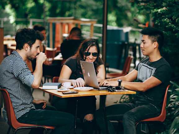Three people sitting at a table with laptops in a cafe.