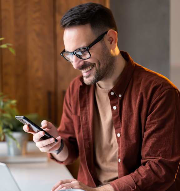 A man in a red shirt is using a smartphone while sitting at a table with a laptop and a cup of coffee.at Montage, Tigard Oregon