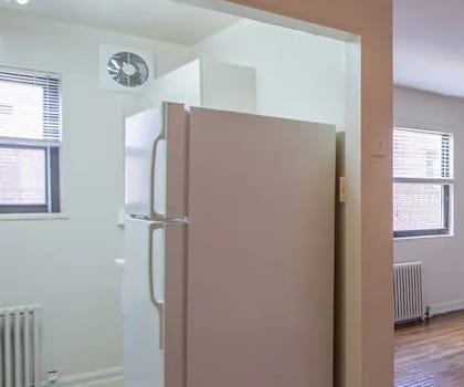 A white refrigerator is in a room with wood floors and white walls.