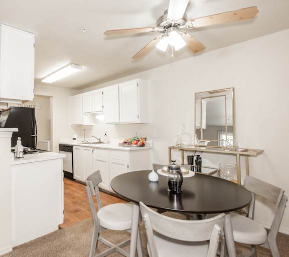 Round kitchen table next to the kitchen with white cabinets and a ceiling fan at Valley River Court in Oregon