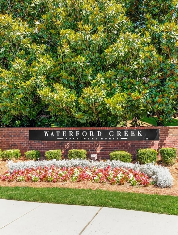 a sign for waterford creek in front of a brick wall with flowers and trees