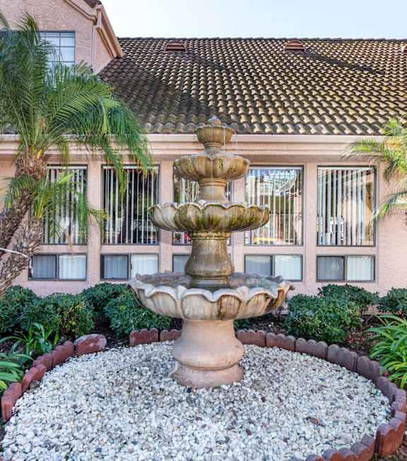 A fountain in the middle of a garden with a building in the background. at Whispering Fountains Diamond Bar, California