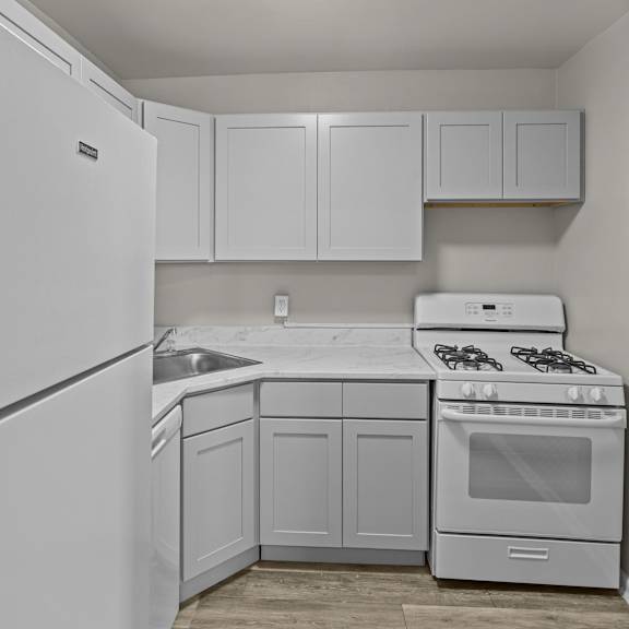 A white kitchen with a refrigerator, sink, stove, and cabinets at Kensington House, Maryland 20895
