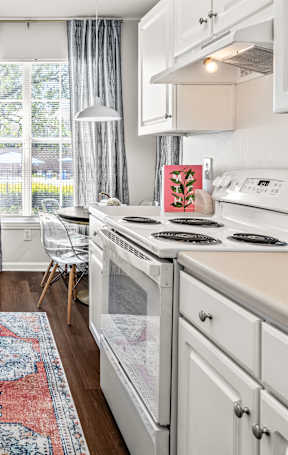 A kitchen with white cabinets and a red rug on the floor.