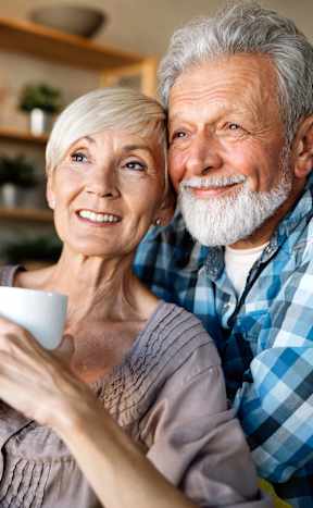 An older couple is sitting together holding a cup.