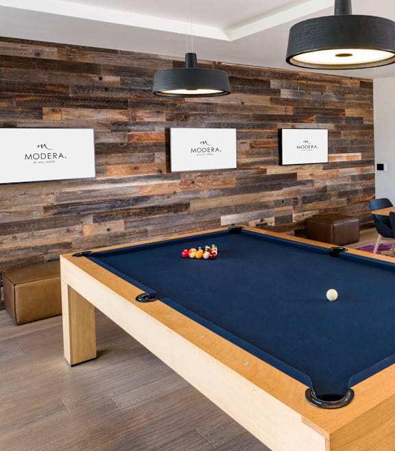 A pool table is in the middle of a room with a wooden wall.