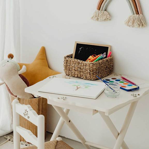 A white desk with a yellow star-shaped pillow and a white chair with a wooden design.