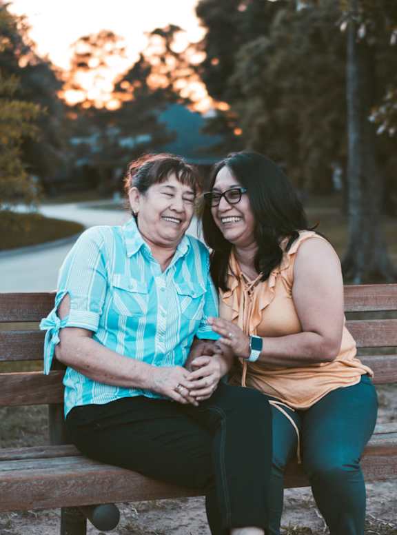 Two women sitting on a bench in a park.
