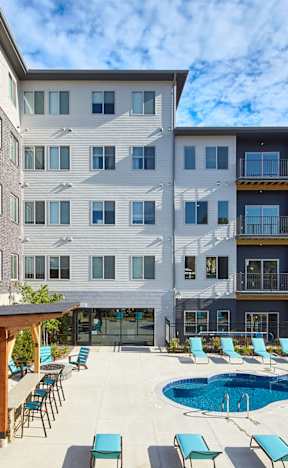 A large apartment complex with a pool and lounge chairs.