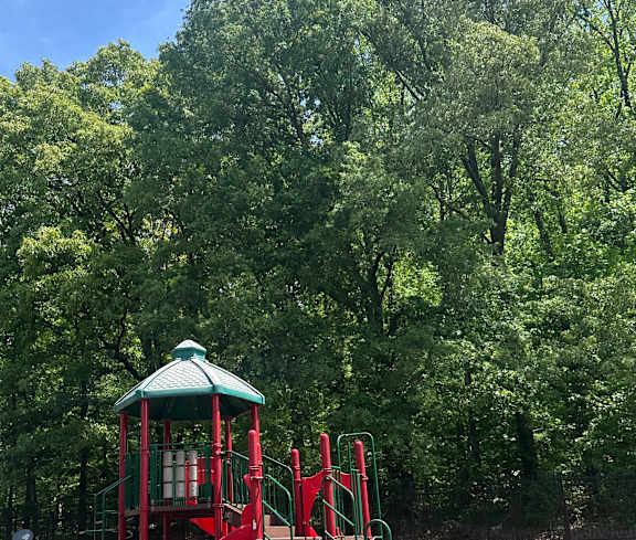 A red playground in front of  trees.