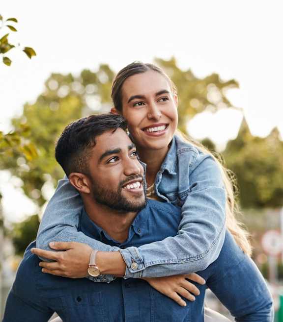 A man is giving a woman a piggyback ride in a park.