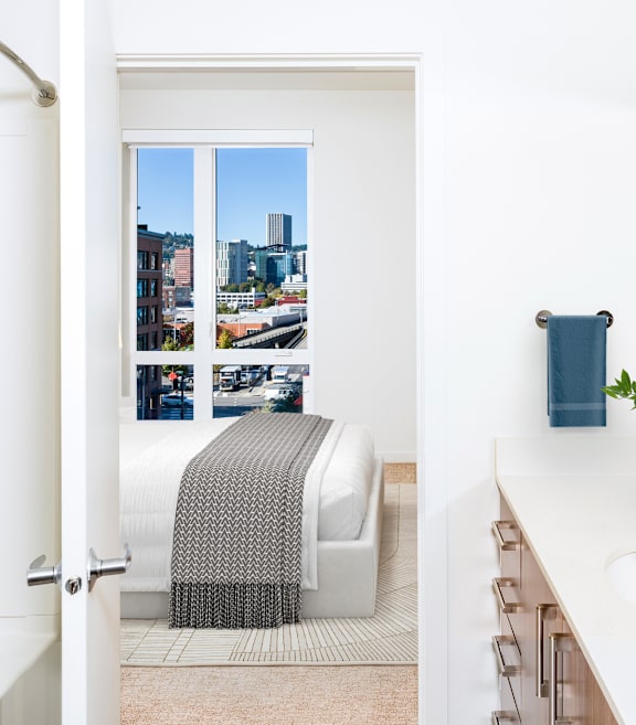 A bedroom with a large bed, a painting on the wall, and a view of the city.
