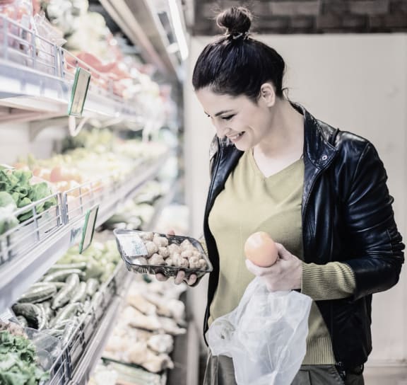 a woman shopping in a grocery store holding an egg and a basket of food