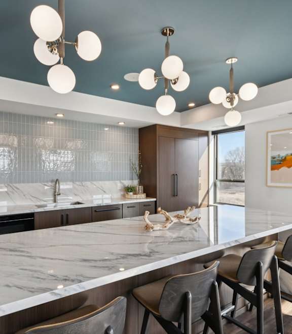 A modern kitchen with a marble countertop and bar stools.