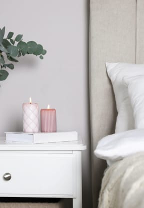 a bedroom with white bedding and a white nightstand with a pink pillow and a plant