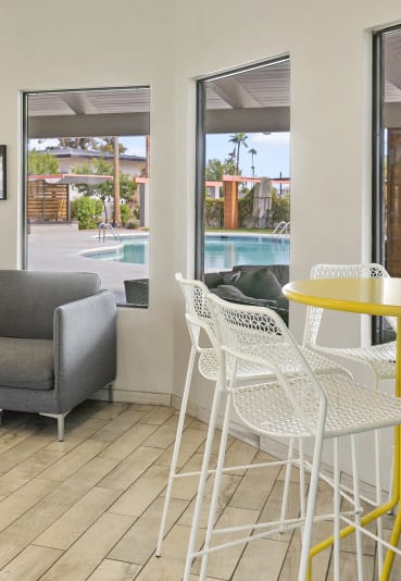 Contemporary resident lounge at Sentry Apartments features a gray sofa, yellow bar tables, and pool views through large windows.
