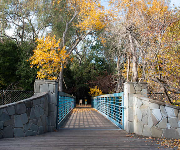 A stone bridge with a blue railing leads across a body of water.