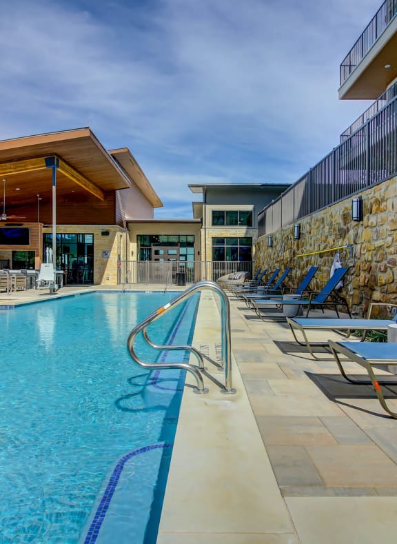 a swimming pool with lounge chairs and a building with a stone wall