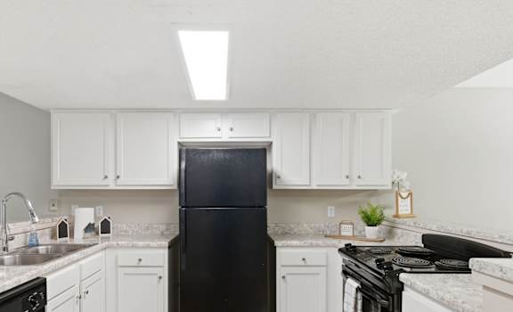 A black refrigerator in a kitchen with white cabinets and a marble countertop.