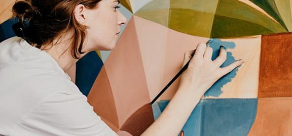 A woman is painting a picture with a paintbrush.