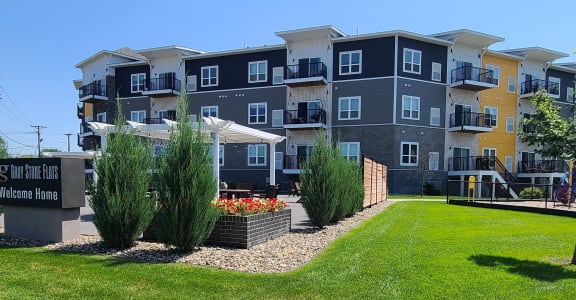 an apartment building with a green lawn and trees in front of it
