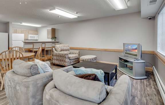 Community room with a television, sofa and chairs and kitchette.