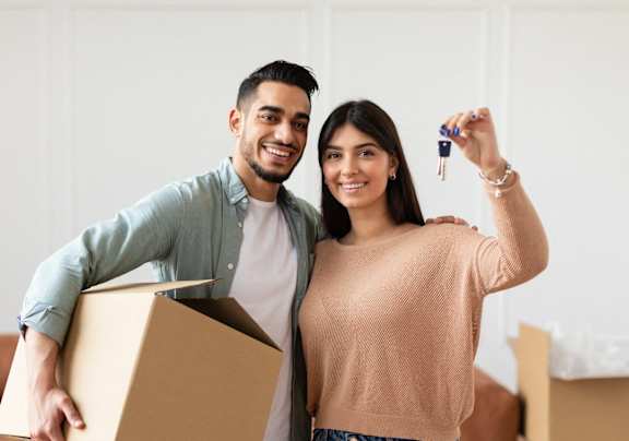 A man and woman are standing in a room with boxes, holding a key and a box at Villas at San Dorado, Oro Valley, AZ, 85737