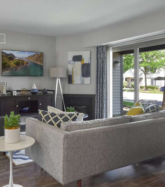 A living room with a grey couch, a grey chair, a white table, and a painting on the wall.