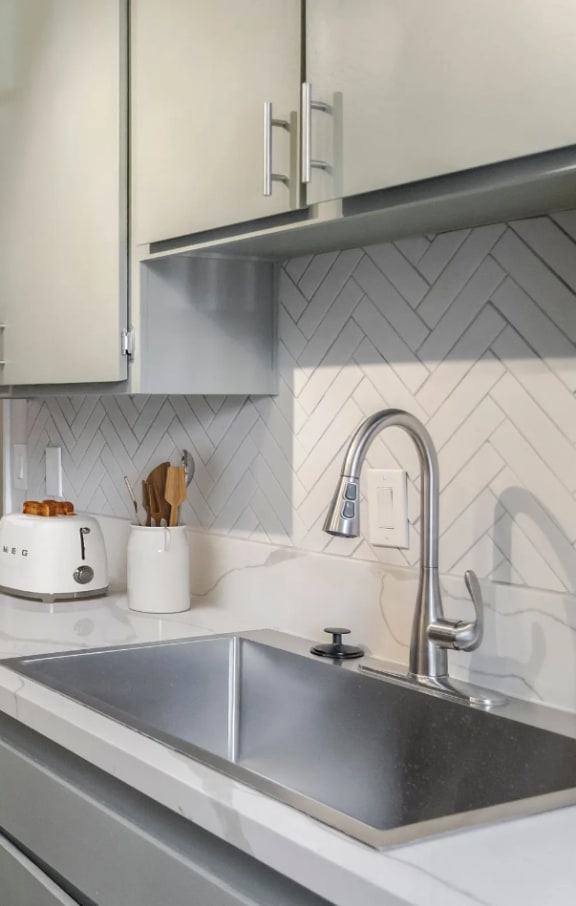 Kitchen with herringbone tile and marble countertops with sage green cabinetry and smeg toaster at Summer Meadows in Riverside, CA