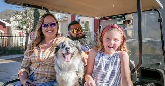 A woman and a girl are sitting on a golf cart with a dog.