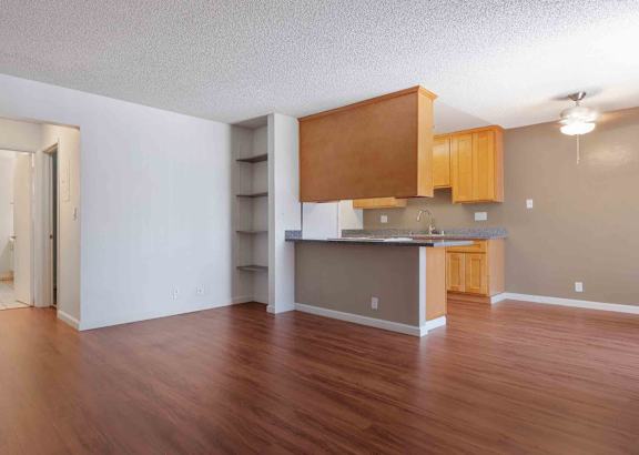 San Jose CA Apartments - Village of Taxco - Spacious Living Area with Open-Concept Floorplan with Wood-Style Flooring, Wooden Cabinetry, White Walls, Storage Shelving, and a Ceiling Fan with a Light