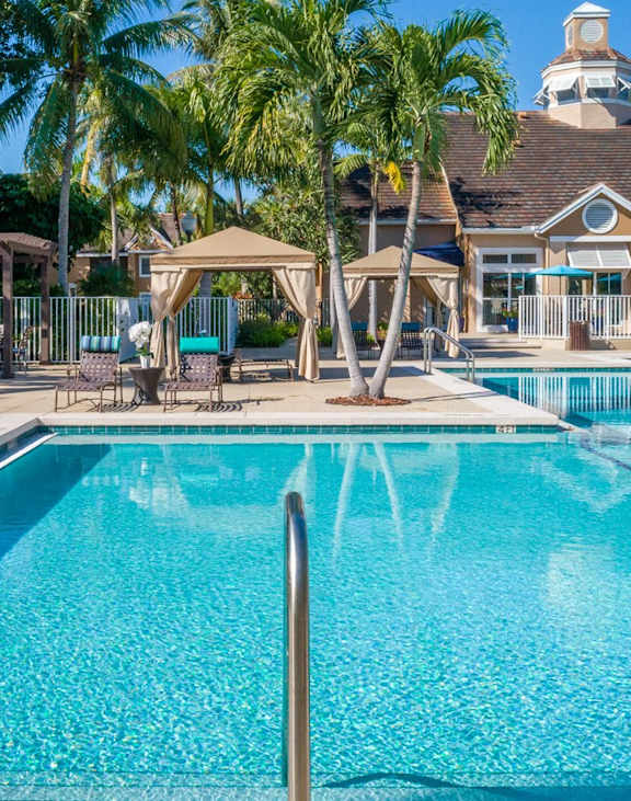 A large swimming pool surrounded by palm trees and a building in the background.