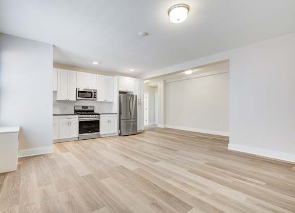 a renovated living room and kitchen with white walls and wood flooring