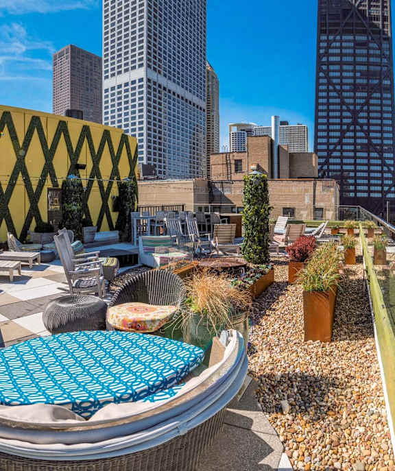 A rooftop patio with a blue cushioned seating area and a yellow geometric building in the background.