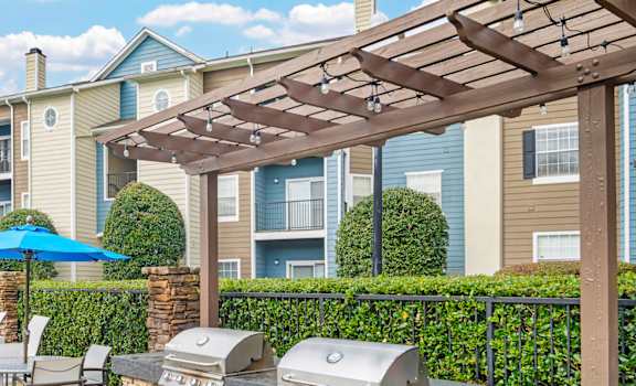 A patio with a grill and chairs under a pergola.