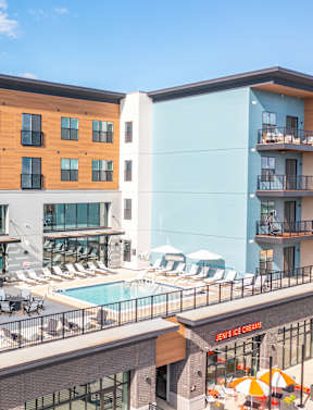 A rendering of a modern apartment complex with a lush green lawn and people enjoying the outdoors. at The District at Deerfield Residences Apartments, Mason, OH, 45040