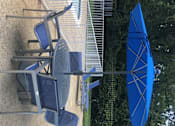 Thumbnail 29 of 29 - A blue umbrella is next to a pool with a chair underneath it.