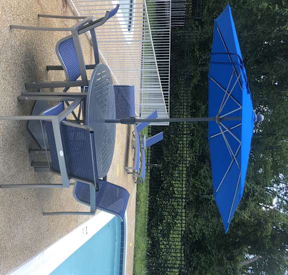 A blue umbrella is next to a pool with a chair underneath it.