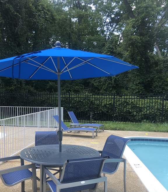 A blue umbrella is next to a pool with a chair underneath it. at New Carrollton Woods, Riverdale, MD