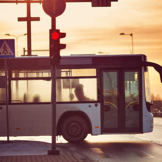 a bus stopped at a traffic light with the sun setting in the background