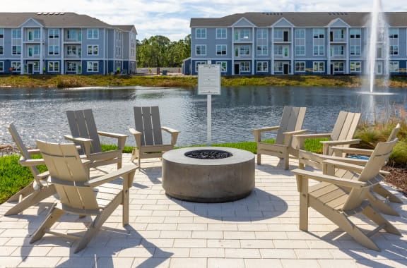 an outdoor patio with chairs around a fire pit and a pond