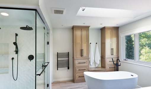 A modern bathroom with a glass shower stall, a white bathtub, and wooden cabinets.