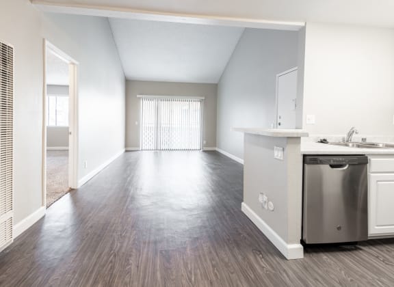 an empty living room and kitchen with stainless steel appliances and wood flooring