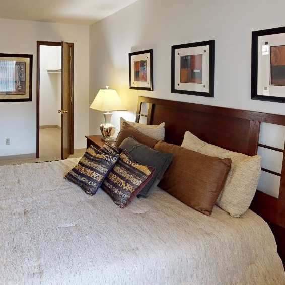 Bedroom in a Regency Woods model unit, featuring a large bed with pillows, a lamp, side table, and a walk-in closet in the background.