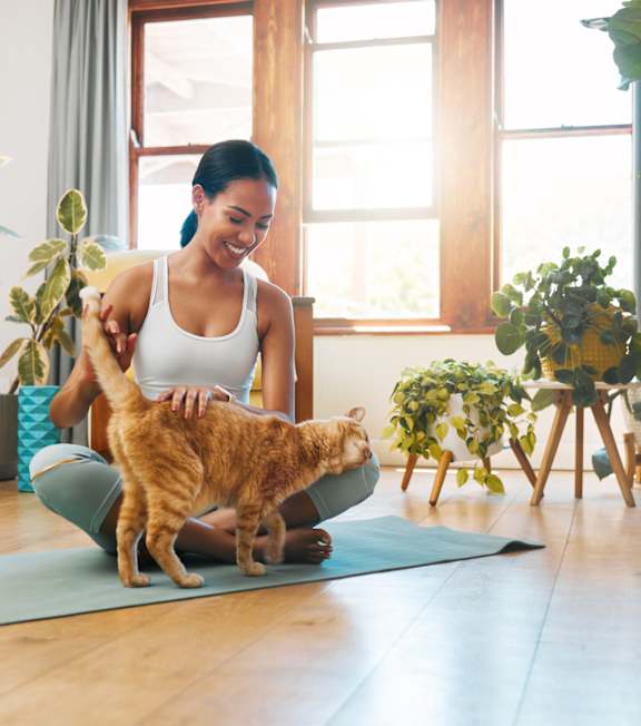 A woman is sitting on a yoga mat with her cat.