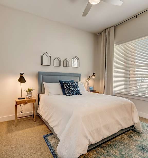 A bedroom with a bed, a nightstand, and a window with blinds.