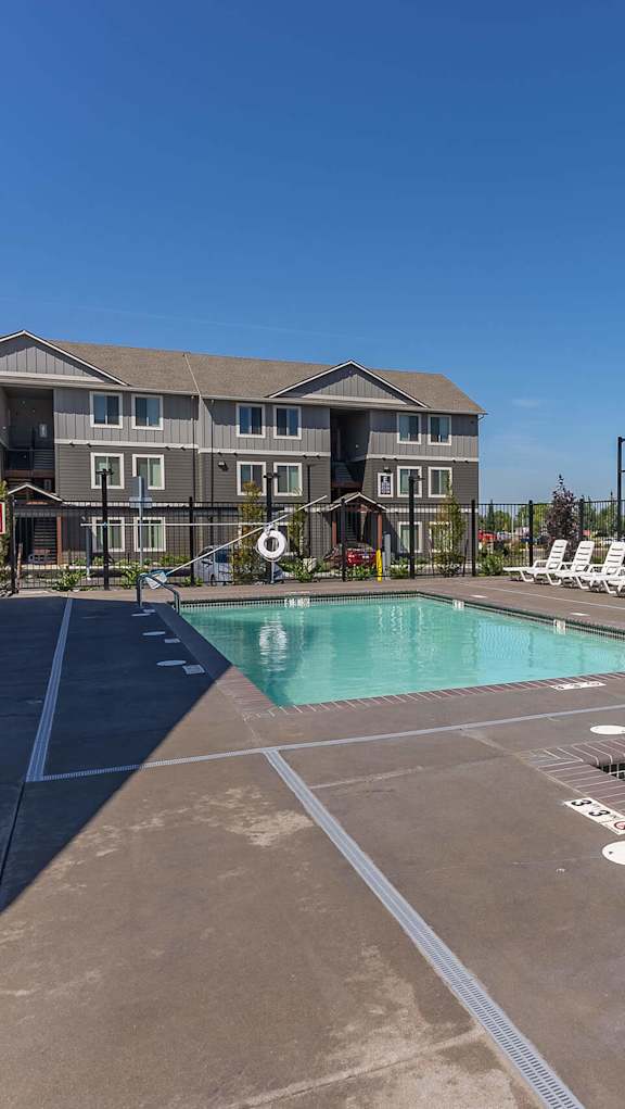 A large outdoor swimming pool with lounge chairs and a building in the background at Cascade Place Apartment Homes, Molalla, OR, 97038