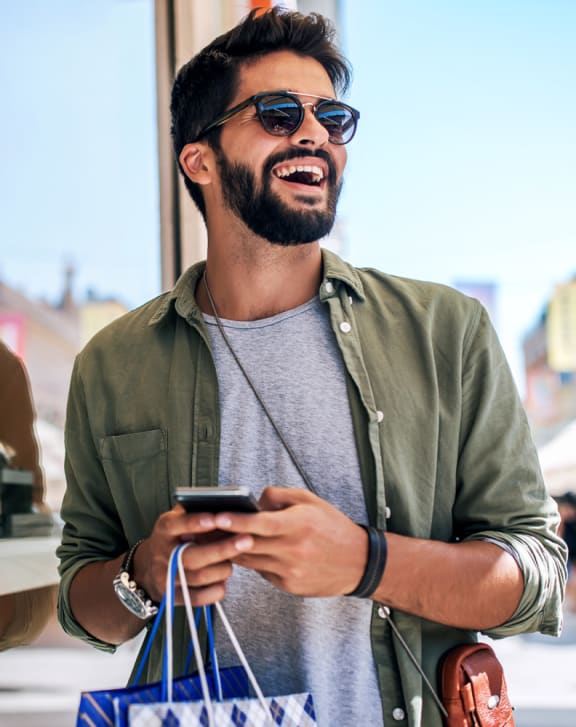 a man looking at his cell phone while holding shopping bags at Novella Arcadia, Phoenix, AZ 85018